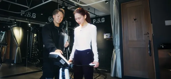 体組成計に乗る女性とそれを見るトレーナー